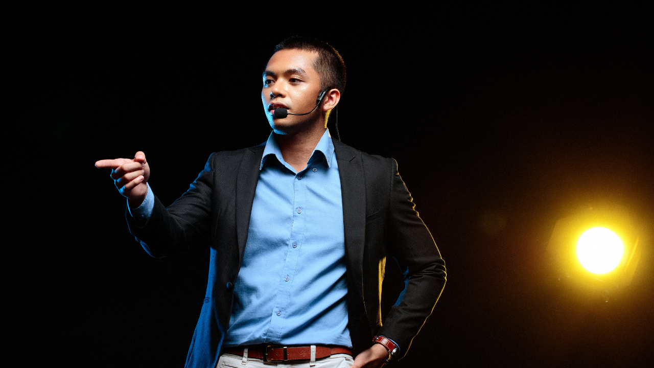 Man standing on stage speaking confidently.