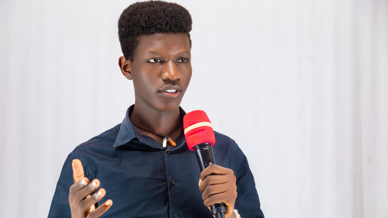 A young man delivers a speech with confidence, gesturing as he speaks into the microphone. His presence reflects strong communication skills, the kind of impact Gaby often encourages when coaching professionals to share their voices.