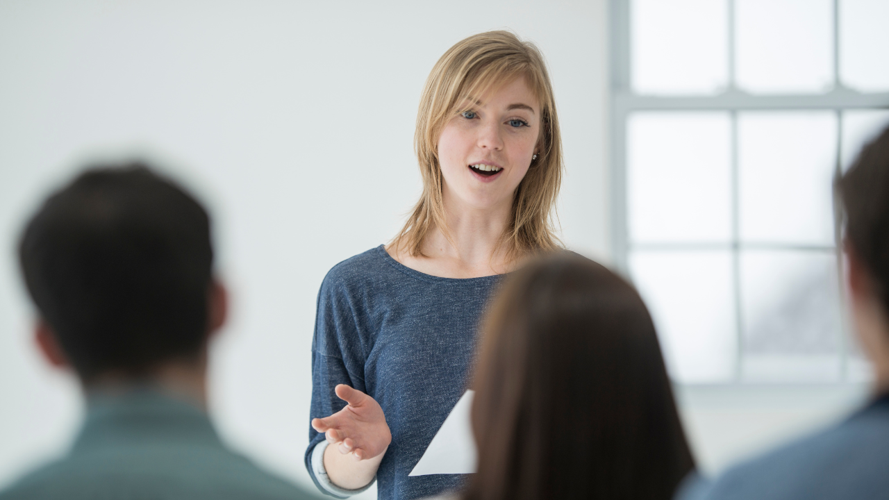 A woman presents to a small group, engaging her listeners with an open and approachable style. This type of effective communication is at the heart of what Gaby emphasizes, connecting authentically with others.
